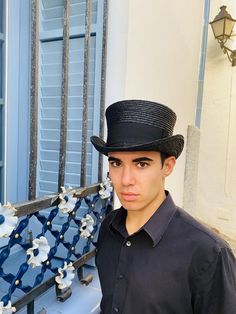 a young man wearing a black hat standing in front of a blue building with shutters