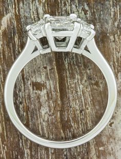 a three stone diamond ring sitting on top of a piece of wood with the center stone missing