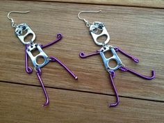 two pairs of purple wire hang from silver hooks on a wooden surface, with the shape of a pair of scissors in the middle