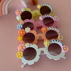 three pairs of sunglasses with flowers on them sitting next to a rainbow shaped object in the background