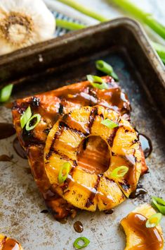 grilled pineapple on a baking sheet with brown sauce and green onions in the background