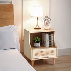 a night stand with books and a lamp on it next to a bed in a bedroom