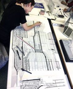 a woman sitting at a table working on architectural drawings