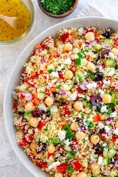 a white bowl filled with salad next to two bowls full of dressing and seasoning