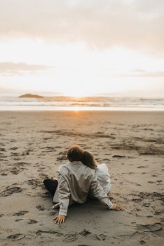 a woman is sitting on the beach at sunset