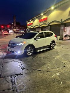 a white car is parked in front of a store at night with its lights on