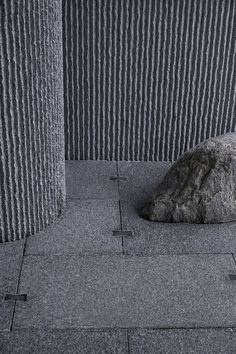 a large rock sitting on top of a sidewalk next to two tall buildings with vertical striped walls in the background