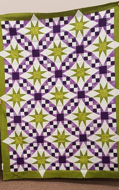 a green and purple quilt hanging on a wall