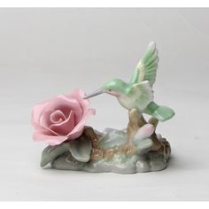 a pink rose sitting on top of a rock next to a humming bird figurine