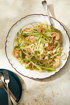 a white bowl filled with pasta and shrimp on top of a table next to a fork