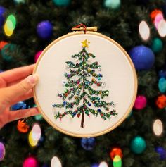 someone holding up a christmas tree ornament in front of a decorated christmas tree