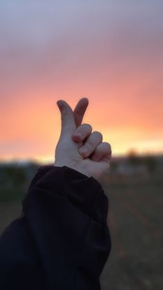 a person holding their hand up in the air at sunset or dawn with an orange and pink sky behind them