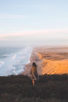 a woman standing on top of a lush green hillside next to the ocean