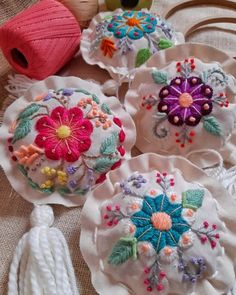 four embroidered flowers are sitting on top of some white doily with tassels