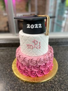 a graduation cake with pink and white frosting on top, sitting on a gold plate