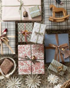 several wrapped presents are sitting on the floor next to other wrapping paper and decorations, including a rocking horse