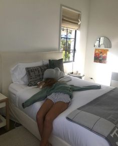 a woman laying on top of a white bed in a bedroom next to a window