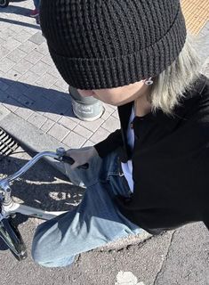 a young man sitting on the ground next to a skateboard wearing a beanie