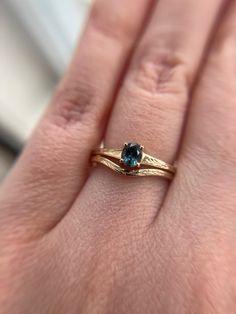 a woman's hand holding a gold ring with a blue diamond