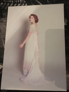 an old photo of a woman in a white dress standing against a wall with her hand on her hip