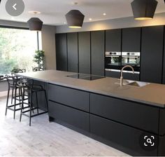 a modern kitchen with black cabinets and counter tops, bar stools in the center