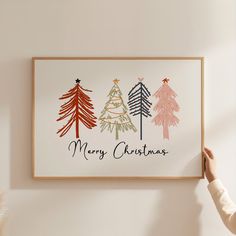 a person holding up a christmas card with trees on it and the words merry christmas