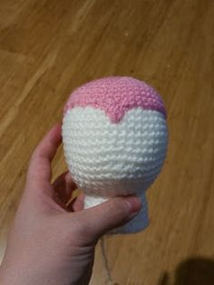 a hand holding a pink and white crocheted heart on top of a wooden floor