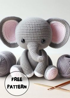 a crocheted elephant sitting next to two balls of yarn with knitting needles nearby