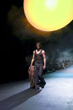 a man walking down a runway in front of a yellow ball