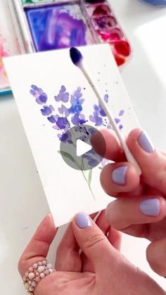 a woman holding a paintbrush in her left hand while painting flowers on a piece of paper