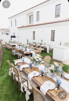 an outdoor dining area with wooden tables and white linens on the grass, decorated with blue and white flowers