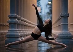 a woman in black leotard doing yoga on the street at night with her arms stretched out