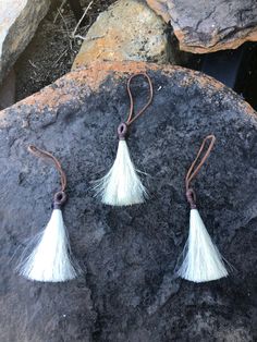 two white tasseled earrings sitting on top of a rock next to some rocks