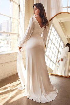 a woman standing in front of a mirror wearing a white dress with long sleeves and an open back