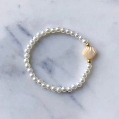 The Shelly Bracelet is here!  Featuring a single Clam Shell in your choice of color on a pearl beaded band paired with a Gold filled hug, finished with our Laguna brand tag. Clam Shell Color Options:  Mint Blue  Purple White Yellow Peach Pink Tan Please measure before you order! Sizing can vary by age.  Bracelets are made with a durable stretch elastic to comfortably slide on and off your wrist. Size Chart: XXS- 5.5" XS- 6" Small- 6.5" Medium- 7" Large- 7.5" XL- 8" Sizing details: To measure wrist grab a string or paper wrap it tightly around wrist in place desired. Then Measure string against ruler add 1/2" to size as beads will tighten the fit once on string.  If you are in between sizes, I would recommend sizing down since they do stretch. Gift wrapping and packaging: All orders come in Pearl And Shell Bracelet, Adjustable Pearl Bracelet With Charm And Round Beads, Adjustable Pearl Beaded Bracelets With Pearl Drop, Pearl White Adjustable Pearl Charm Bracelet, Adjustable Pearl White Beaded Bracelets With Pearl Drop, Adjustable Beaded Pearl Bracelet With Pearl Charm, Adjustable Beaded Pearl Bracelets With Pearl Charm, Beach Pearl Bracelet With Pearl Charm, Adjustable Hand-strung Pearl White Pearl Bracelet