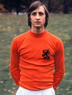 a man in an orange shirt and white shorts standing in front of a green field