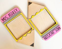 two wooden magnets sitting on top of a white table with pink and yellow writing