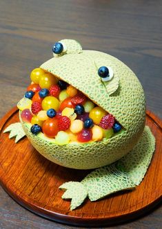 a frog made out of fruit sitting on top of a wooden plate