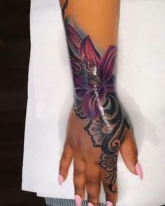 a woman's hand with tattoos on it and a purple flower tattooed on the wrist