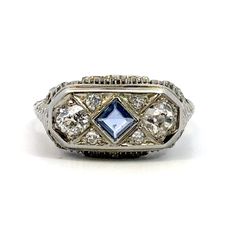 This vintage 18K white gold ring showcases a beautiful blue sapphire and diamond filigree design. The ring is a size 7.75 and features a bezel and prong setting style. The main stone is a natural square-shaped sapphire, and the secondary stone is a diamond. The ring has a vintage feel and is perfect for anyone who loves classic and timeless pieces. The metal purity is 18K, and the style is filigree. This ring is perfect for any occasion and would make a great addition to anyone's jewelry collection. Sold Exactly As Shown 18K @ 3.1grams(gross) Center sapphire measured about 4x3.8mm All 6 diamonds estimated weight about 1.00CT(2 big ones approx 0.90CT & 4 small ones approx 0.10CT) Can be worn both men and women Pre-owned item most likely there will be some minor dents or scratches, we do our Vintage Blue Sapphire Ring With Bezel Setting, Art Deco Blue Sapphire Ring With Center Stone, Vintage Blue Platinum Rings, Art Deco Blue Diamond Ring With Accents, Heirloom Blue Sapphire Ring With Rose Cut Diamonds, Blue Art Deco Diamond Ring With Accents, Vintage Blue Diamond Platinum Ring, Vintage Blue Diamond Ring In Platinum, Antique Blue Sapphire Diamond Ring