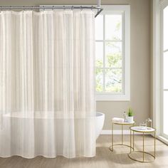 a white shower curtain in a bathroom next to a bathtub and side table with a plant on it