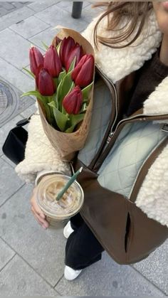 a woman holding a bouquet of red tulips and a drink in her hand