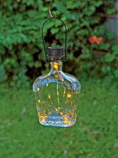 a glass bottle with lights hanging from it's side in front of some grass