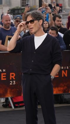 the actor is standing in front of a crowd with his hand on his eyeglasses