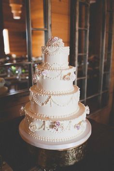 a three tiered white wedding cake with pink flowers on the side and pearls around the edges