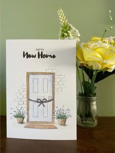 a new home card with yellow flowers in a vase next to it on a table