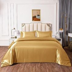 a bed with gold sheets and pillows in a white room next to a painting on the wall