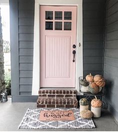 a pink front door and some pumpkins on the porch with a welcome mat next to it