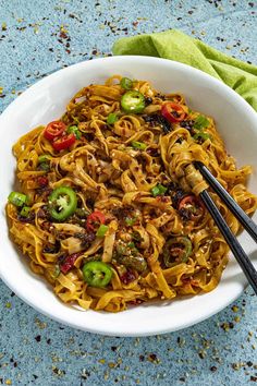 a white bowl filled with noodles and vegetables on top of a blue tablecloth next to chopsticks