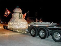 a large snowman is on the back of a semi - truck with christmas lights